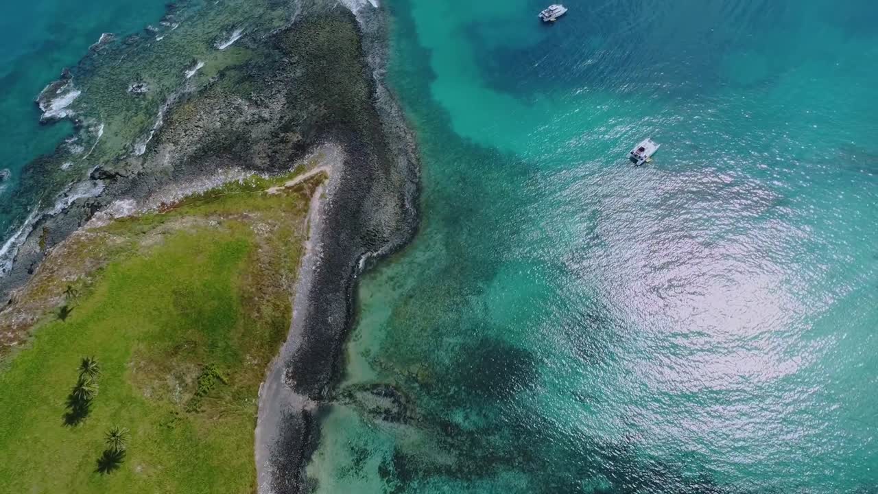 Isola dell'arcipelago di Abrolhos al largo della costa di Bahia in Brasile con una barca che naviga nelle limpide acque tropicali dell'oceano, mostrando una vivace vita marina e un ambiente naturale, ripresa aerea dall'alto con rotazione e avanzamento