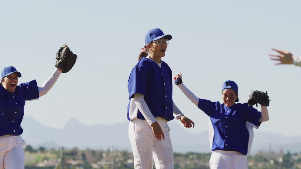 Squadra mista e felice di giocatrici di baseball che festeggiano dopo la partita, abbracciandosi e lanciando i guantoni