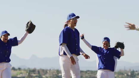 happy diverse team of female baseball players celebrating after game, embracing and throwing gloves