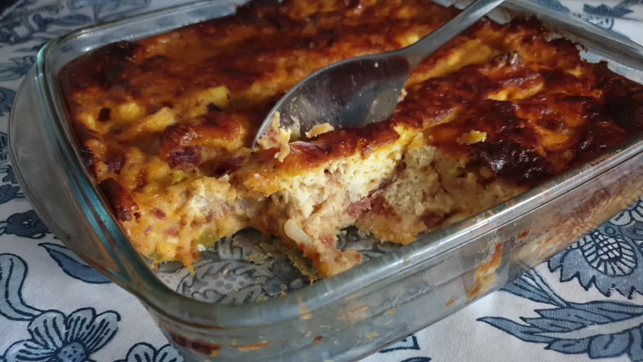 tocino caliente - tarta salada horneada con quiche de jamón cubierta con mucho queso cheddar que se recoge con una cuchara de acero inoxidable para servir la cena de navidad