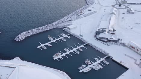 Fishing-boats-docked-safely-on-floating-jetty-in-small-arctic-port,-aerial