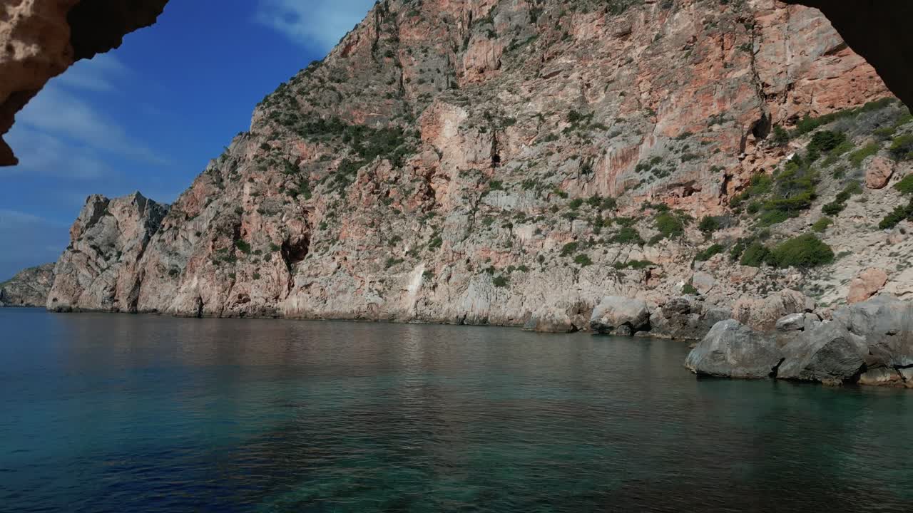 The drone is flying through a hole in a rock cliff at the sea in Ibiza Spain Aerial Footage 4K