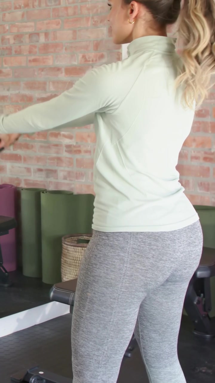 Video verticale: Donna con un top verde chiaro che si china e oscilla una kettlebell con un partner in palestra