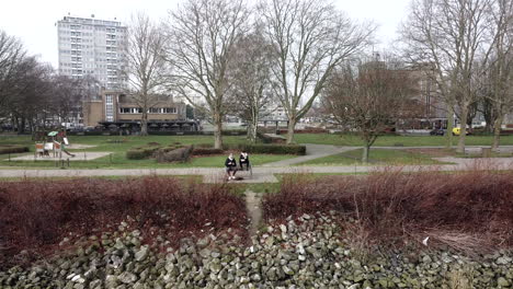 aerial drone flight over river beside two mens sitting on bench in park