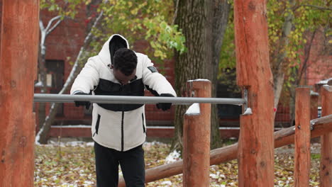 black man resting while holding iron bar in front with head bowed, dressed in warm fleece jacket and gloves, recovering from workout in winter, brick residential building in background