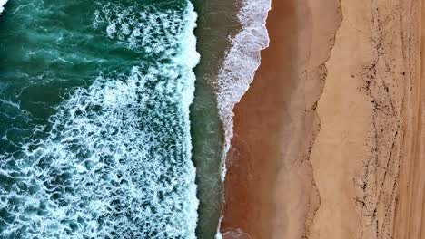 a beach with a wave coming in to the shore and a sandy beach with a green ocean and a sandy shore