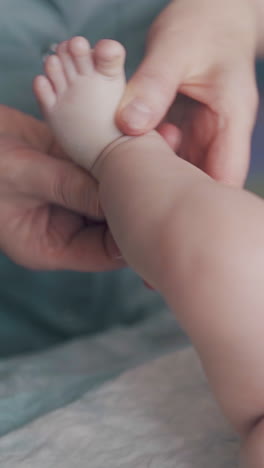 small baby boy in white diaper lies on changing table and professional nurse performs legs massage close view