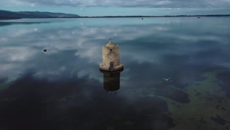 alte spanische mühle in der lagune der inselstadt orbetello in der nähe des monte argentario und des maremmaparks in der toskana, italien, mit blauem himmel und ruhigem blauem wasser