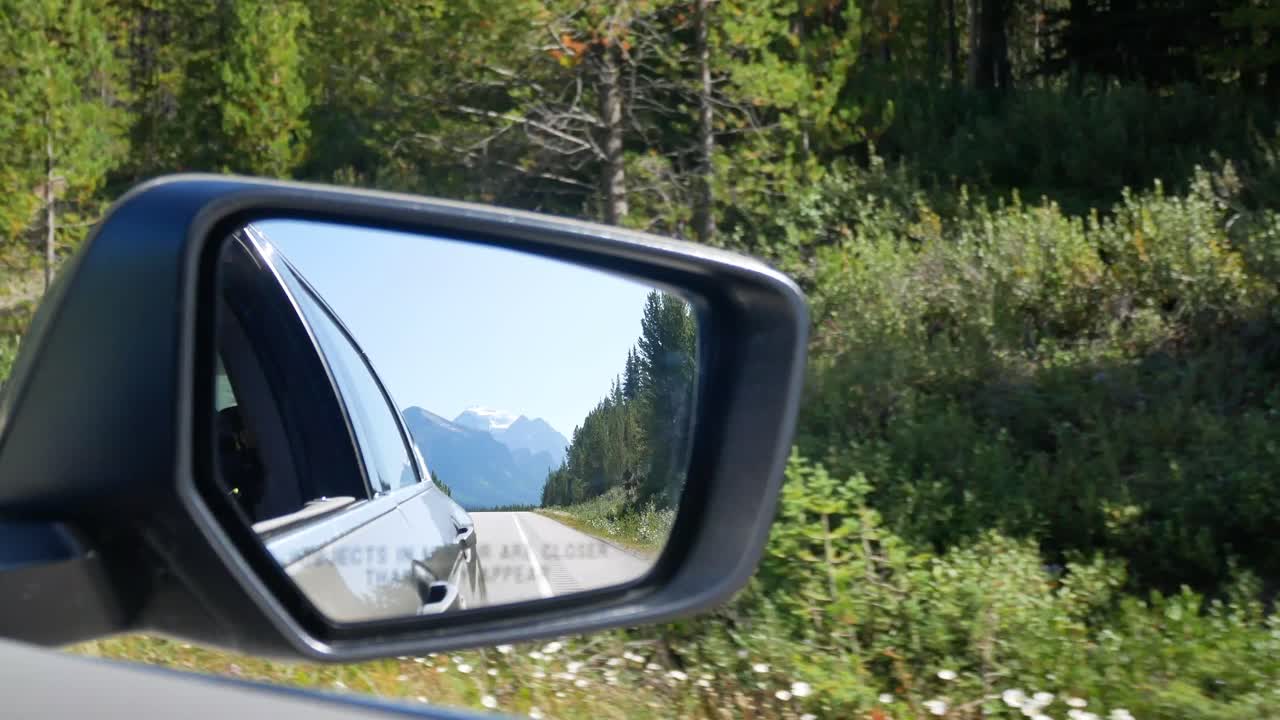 View of side mirror of the moving car on the local road moving along the local way through the Banff National park in Alberta, Canada