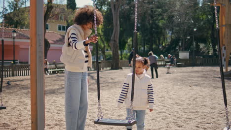 niña va a swing madre en el patio de recreo de los niños. ocio familiar.