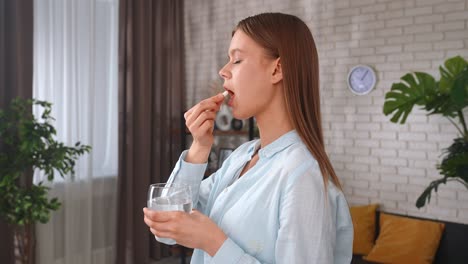 young woman taking a pill with water in the morning a young woman takes a pill and drinks water from a glass symbolizing health wellbeing and daily routine concept of healthy lifestyle taking vitamins for beauty of skin and hair