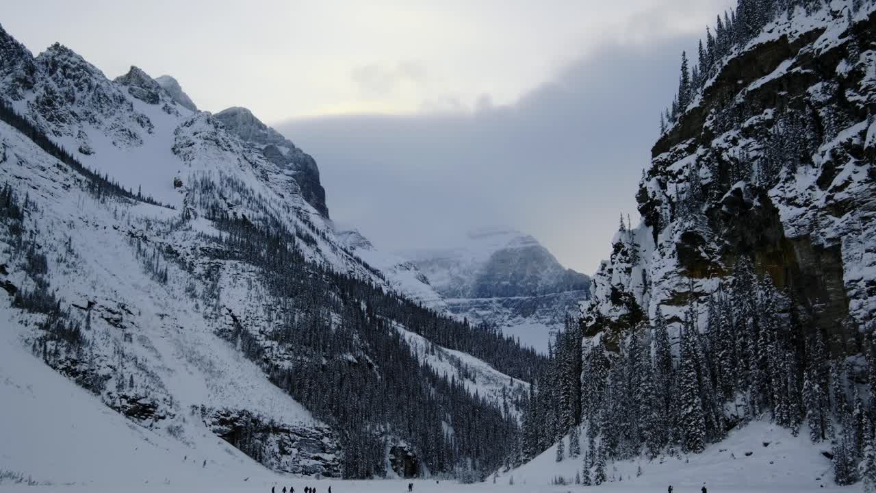 Turisti al Lago Louise ghiacciato, con la foresta sempreverde e le montagne canadesi. Inquadratura ampia