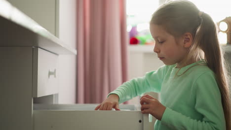 Little-girl-opens-drawer-and-wonders-of-folder-in-room