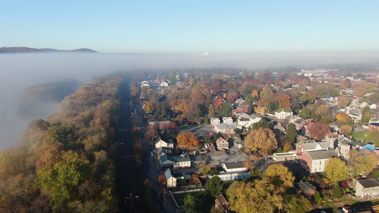 la antena ascendente revela la ciudad en el colorido follaje otoñal, rodeada de niebla y nubes en la luz dorada de la mañana