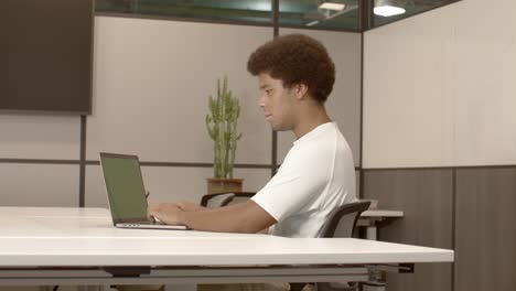 hombre afroamericano de 20 años escribiendo en una computadora en una oficina con un video dolly de izquierda a derecha