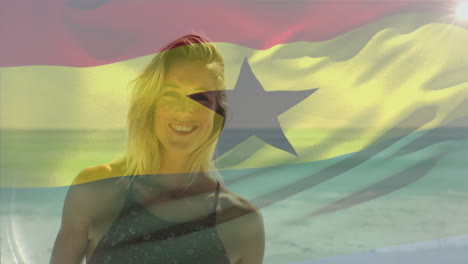 animación de agitar la bandera de ghana sobre una mujer caucásica sonriente de pie contra el mar en la playa