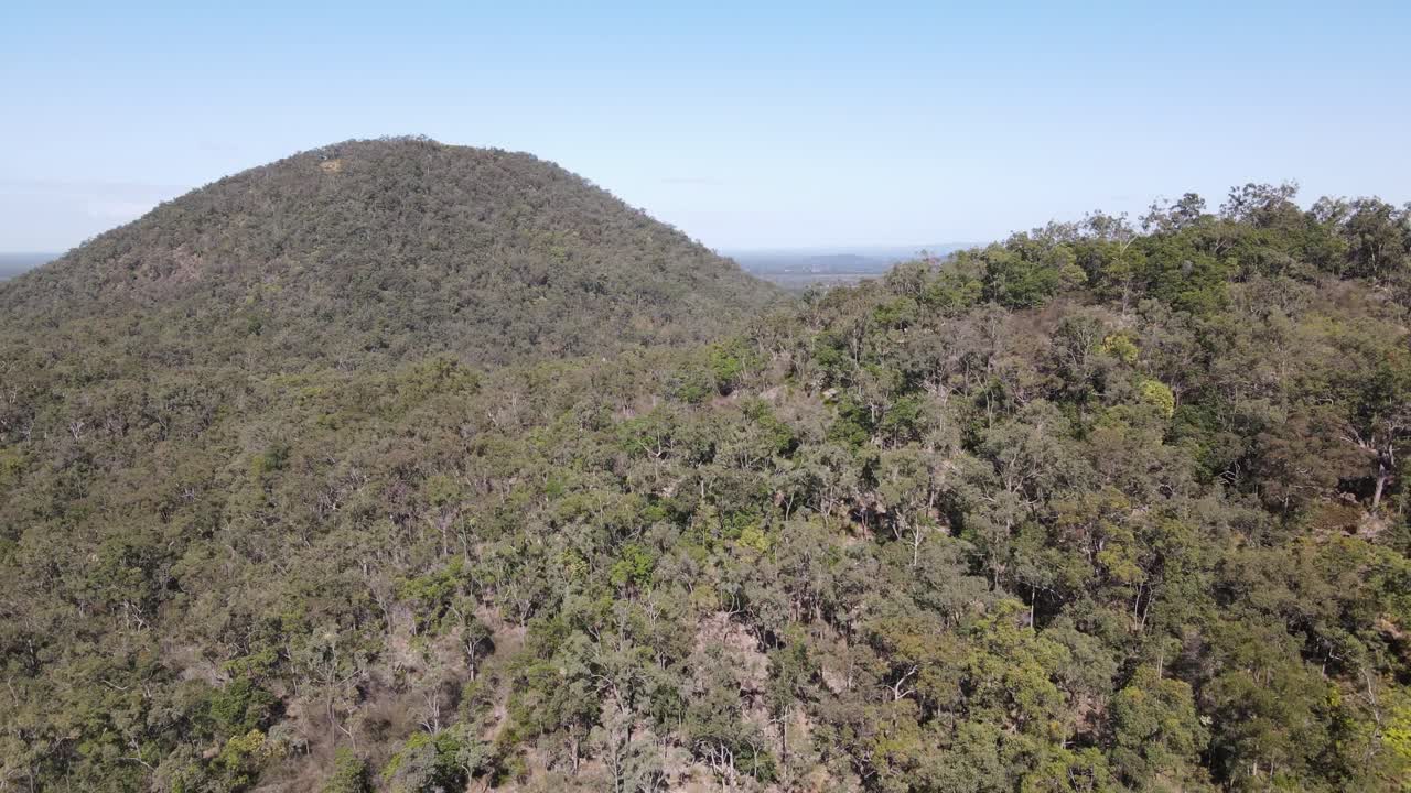 Drone aerial moving towards the lush glasshouse mountains on a sunny day