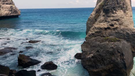 Aerial-view-of-the-crystal-blue-water-of-diamond-beach-in-Nusa-Penida,-Indonesia-with-a-prominent-large-cliff-in-the-foreground