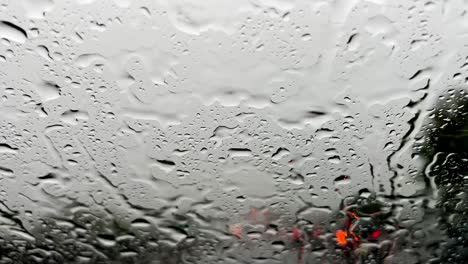 gotas de lluvia en el parabrisas y luces rojas borrosas del tráfico de automóviles en el fondo, limpiaparabrisas limpiando el parabrisas de la lluvia torrencial