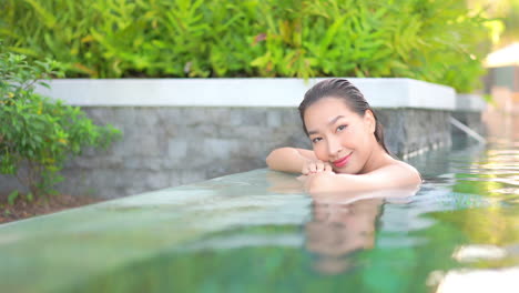 close-up of a pretty young woman in a swimming pool, leaning along the edge surrounded by lush tropical plants