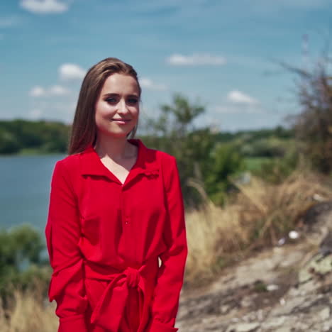 portrait of a beautiful woman on nature background. attractive young model in red dress with long hair standing near the river and smiling.