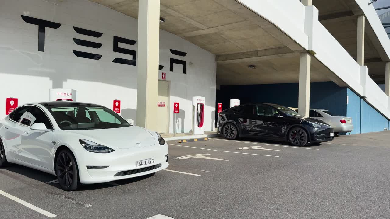 White electric car parks at charging station under covered structure, daylight, wide angle, steady camera