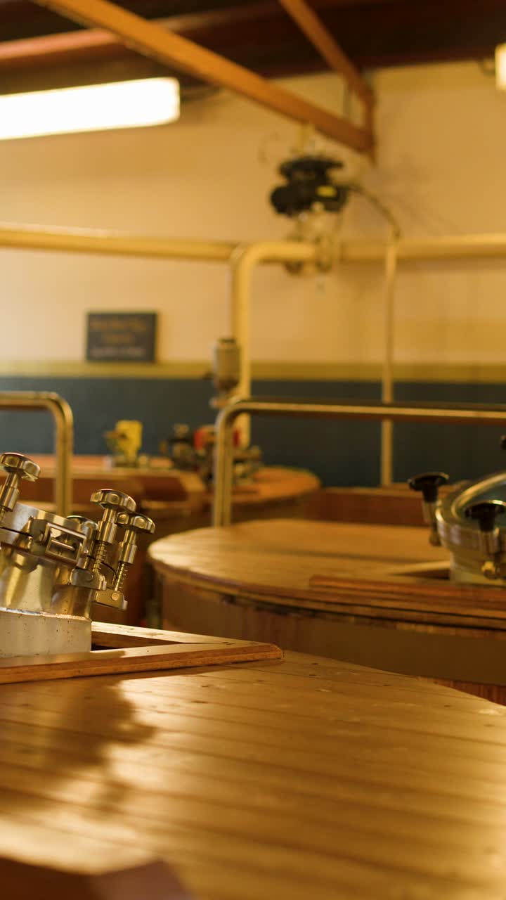 Interno di distilleria illuminato calorosamente con tini di fermentazione in legno, portelli metallici e attrezzature di fermentazione visibili