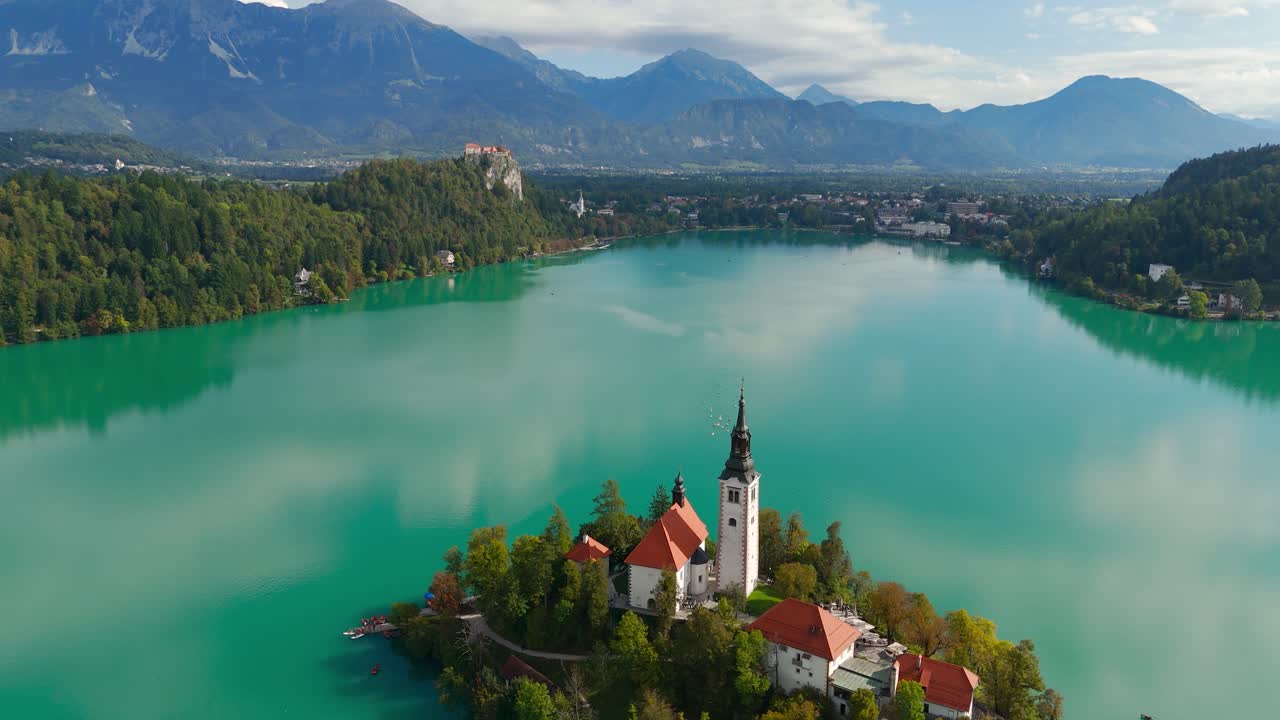 Ampia ripresa aerea inclinata verso il basso che rivela l'isola e il castello del lago di Bled incorniciati da foreste e montagne in Slovenia