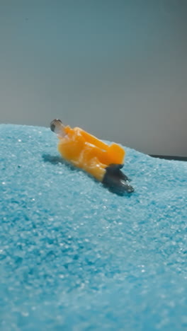 figure of man in yellow coat standing near sandy heap on grey background. figurine with briefcase falling on blue sand shuddering from quakes macro