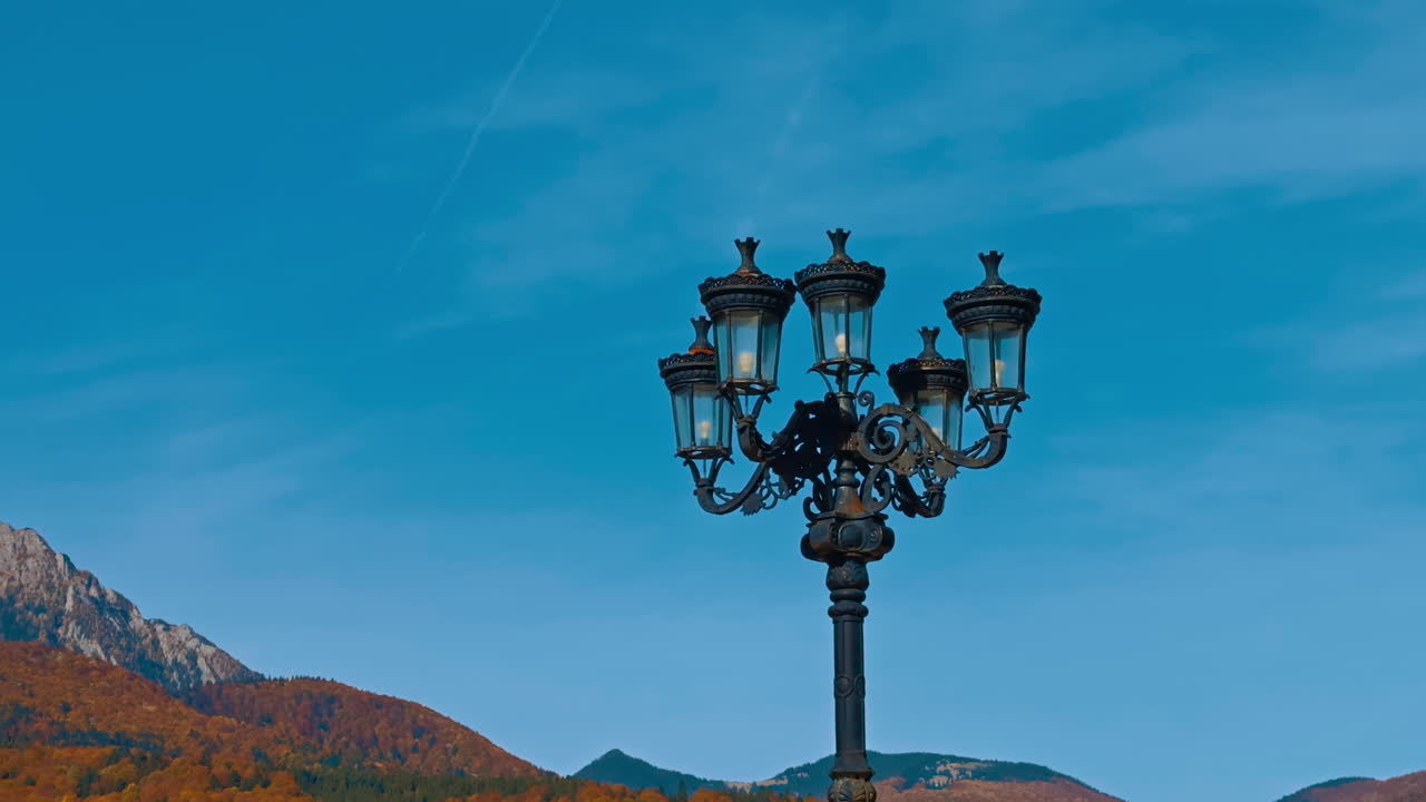Two black street lamps of old style. Low angle view. Mountains in sunny autumn daytime at backdrop.