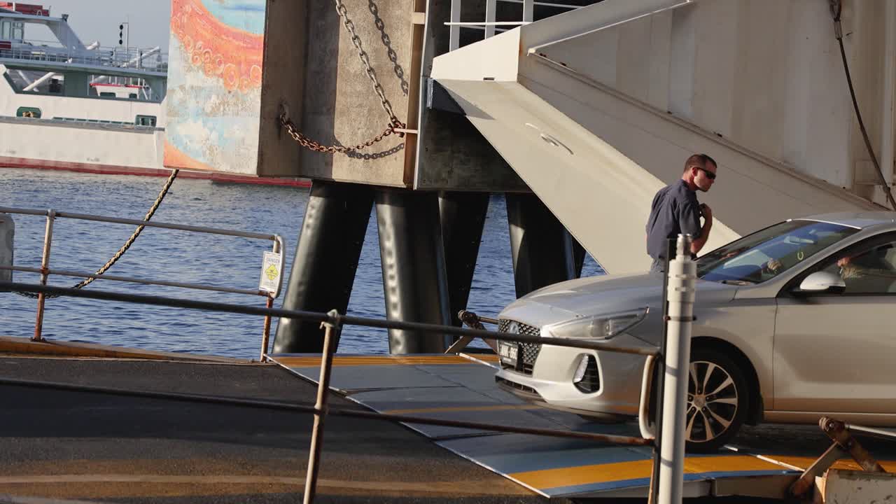 Cars and a truck exit a ferry ramp at Bellarine, Victoria. The scene captures a busy dockside environment with clear, natural lighting