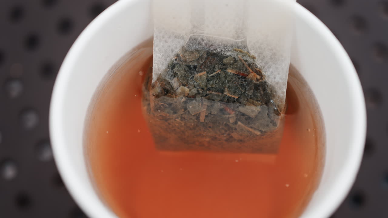 Close up of a tea bag steeping in hot water, releasing rich colour and aroma