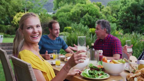 mujer caucásica haciendo un brindis girando y sonriendo durante la comida de celebración familiar en el jardín
