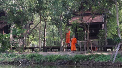 monks in orange robes walking along a wooden bridge