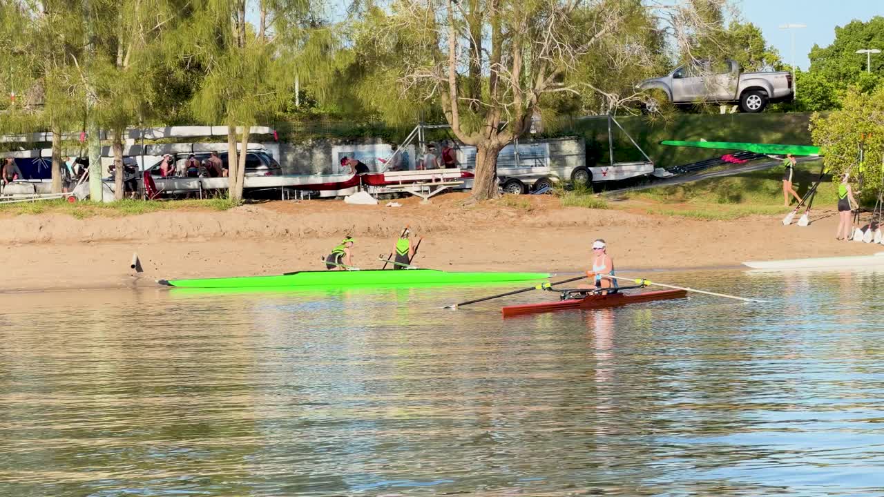 Sportsudøvere ror i sculler-både på roligt flodvand på en solskinsdag i Gold Coast