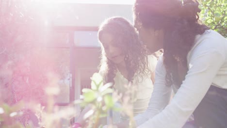 Mixed-race-mother-and-daughter-gardening-in-sunny-garden,-watering-plants