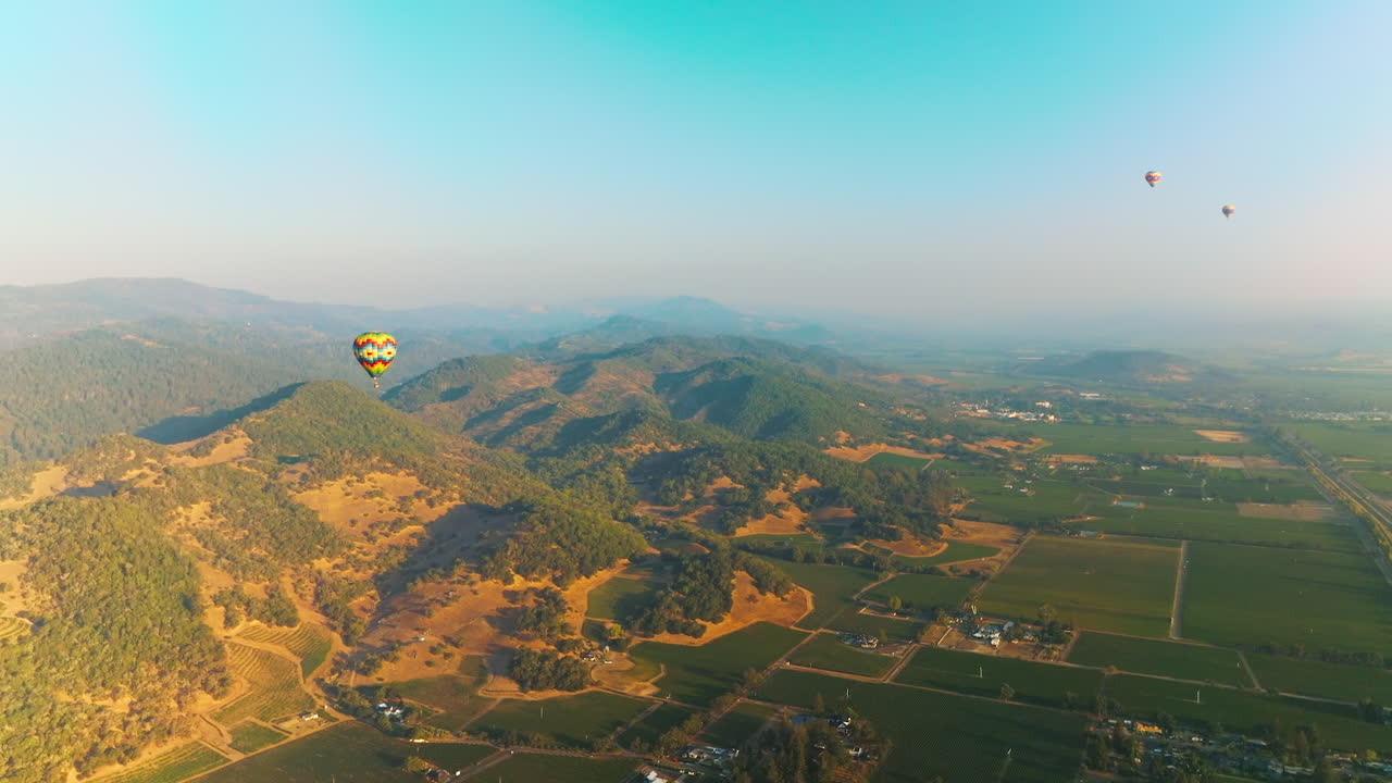 Three hot air balloons in the clear blue skies over amazing scenery. Flying aerostats in green valley of Napa, California, USA.