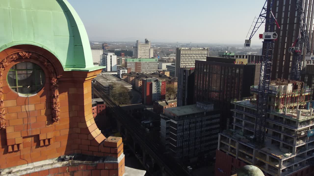 vuelo de arial drone pasando por la estructura de la cúpula verde de la torre del reloj en el edificio kimpton en oxford road en el centro de la ciudad de manchester con vistas a nuevos desarrollos en construcción