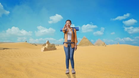 full body of asian female hiker with mountaineering backpack looking at camera and making stop hand sign while traveling in pyramid of giza