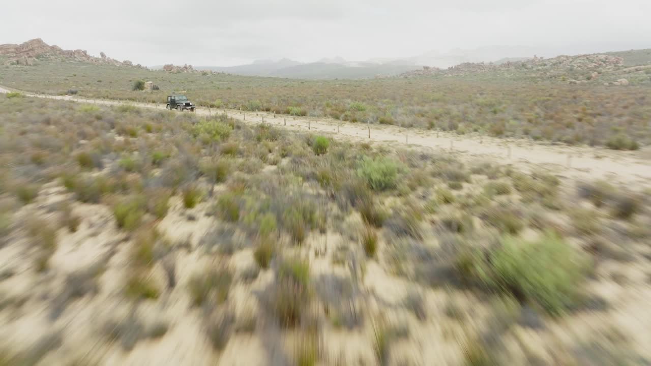 Drone flies fast over desert landscape in Cederberg Wilderness Area south africa and Crosses a road where a black off-road vehicle is driving - scenic landscape