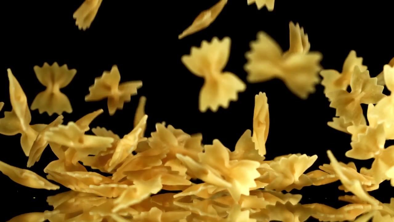 Pasta farfalle secca che cade al rallentatore su sfondo nero.