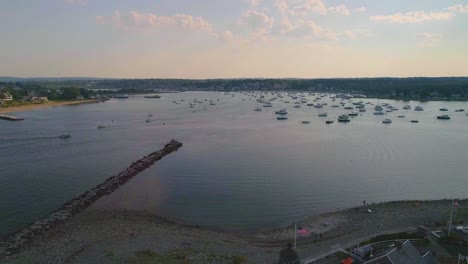 Massachusetts-Lighthouse-with-an-American-flag,-Harbor-with-lots-of-boats