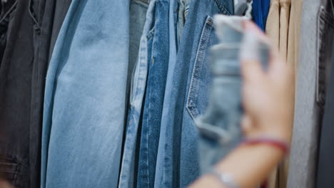 close-up of hand checking denim jeans in clothing store, exploring various shades and styles, showcasing texture and quality of denim, capturing focused shopping experience with casual fashion