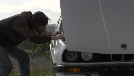 Man-lifts-forward-opening-hood-of-white-car-and-looks-inside