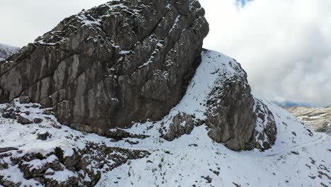 toma aérea volando hacia arriba que revela un enorme acantilado en la cima de la montaña nevada con un hombre parado solo y poderoso en el desierto observando la vasta vista del paisaje que lo rodea