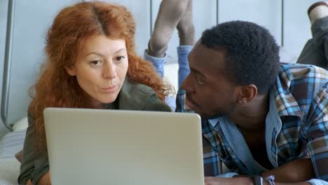 couple lying in bed looking at laptop