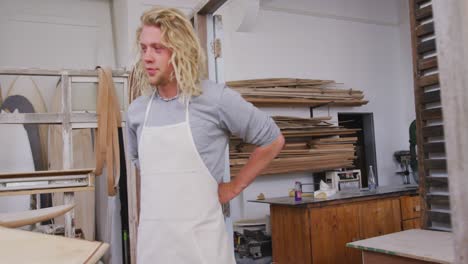 caucasian male surfboard maker putting on a protective apron in his studio