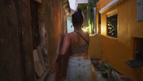 young girl carrying a painting through a bright colourful alley street, with the sun flaring