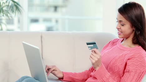 mujer sonriente con una tarjeta de crédito y una computadora portátil en un sofá