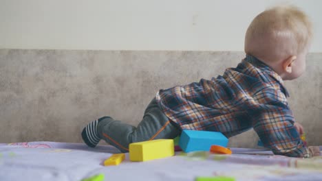 boy-in-shirt-plays-with-color-toy-crawling-on-large-bed